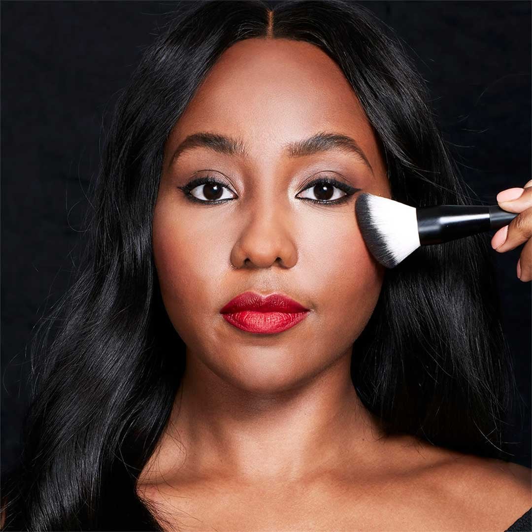 Model applying Lasting Fix Setting and Perfecting Loose Powder by Maybelline to cheekbones.