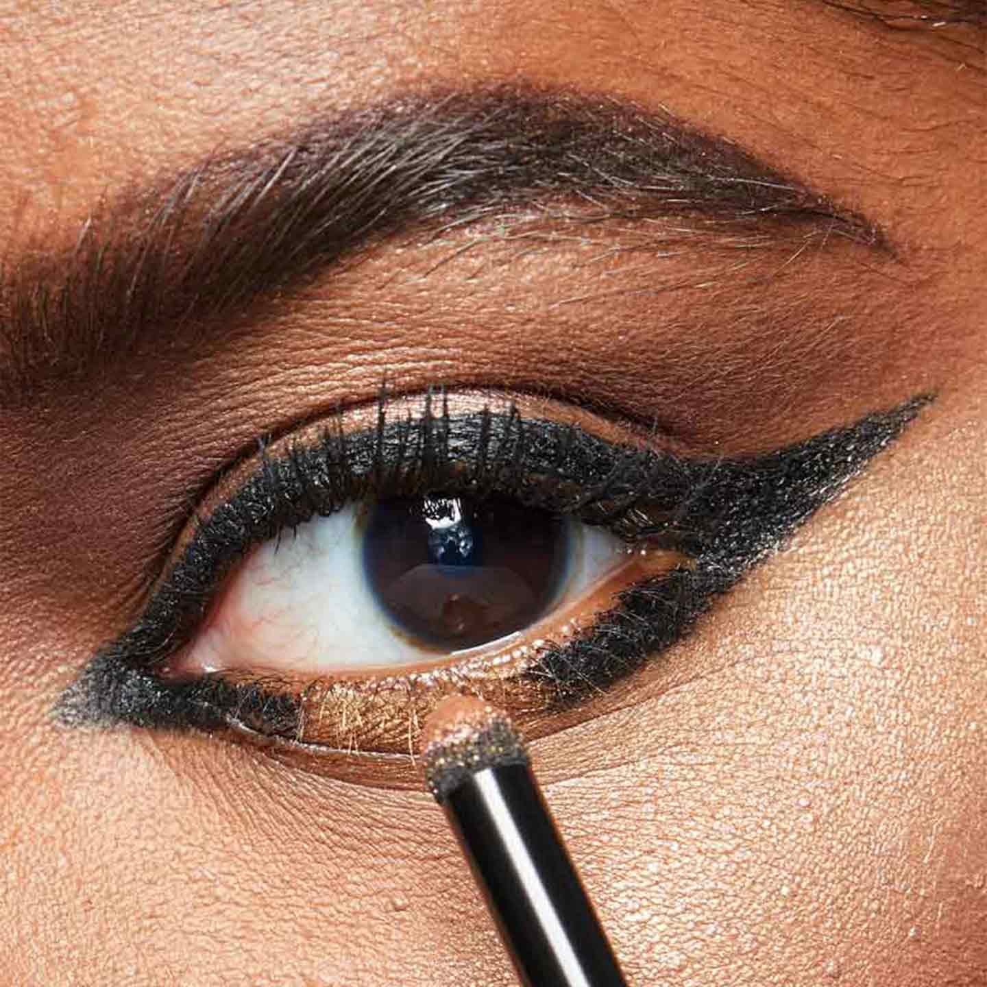 Model creates an open winged eyeliner look with gold eyeshadow by Maybelline.