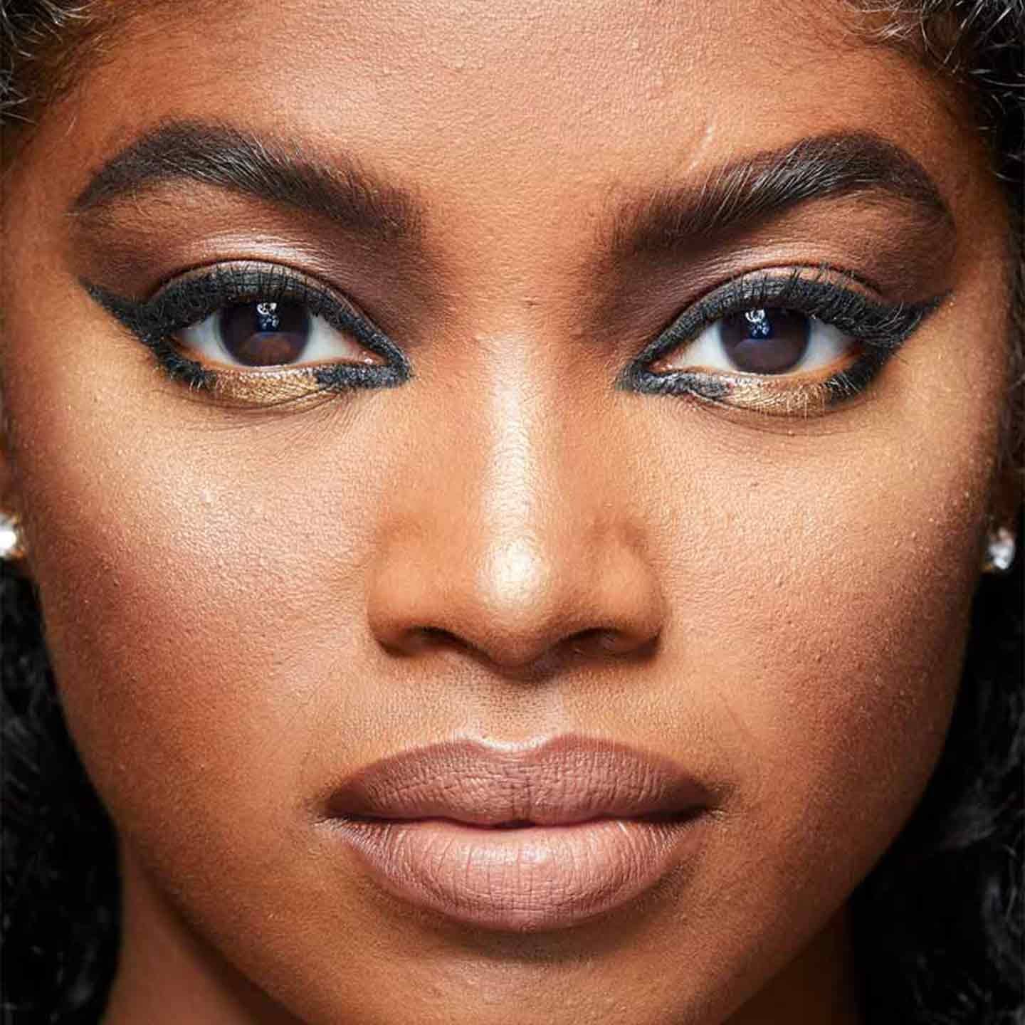Model wears an open winged eyeliner look with black liner and gold shadow by Maybelline.