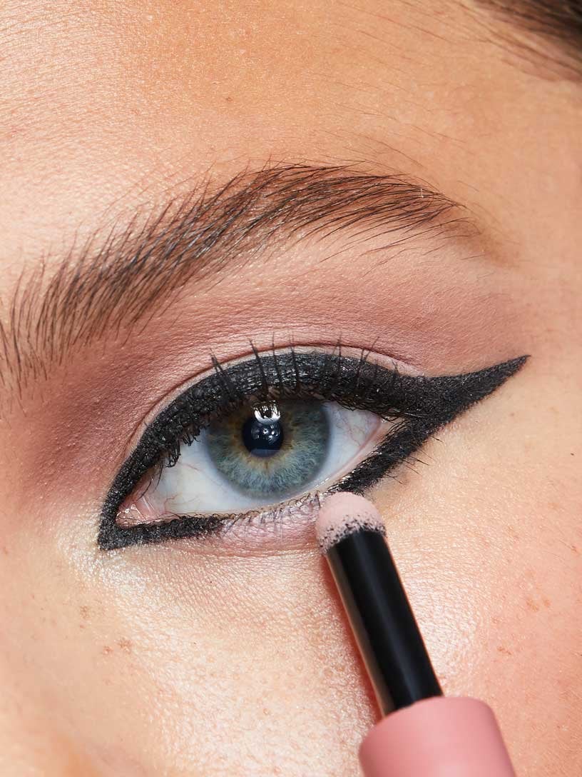 Model applies pink eyeshadow to her winged eyeliner look for an open wing effect.