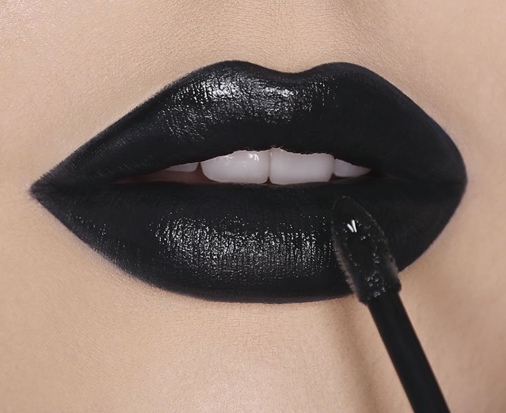 Lip macro of model with fair skin tone applying black lipstick by Maybelline.
