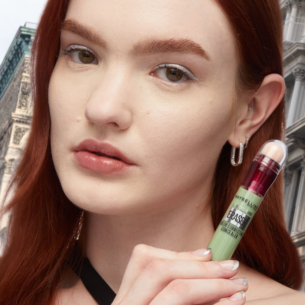 Model holding Instant Age Rewind Eraser Color Correcting Concealer in shade Green